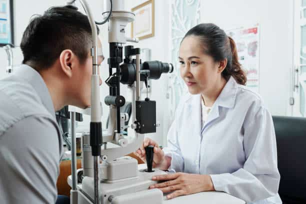 Asian female optometrist looking through the special medical equipment and examining her patient's eyesight at hospital