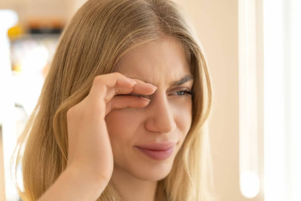 A woman is rubbing her eyes because she is experiencing dry eye syndrome.