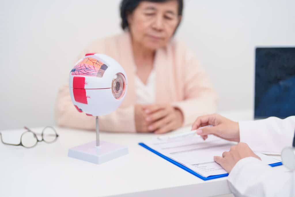 An elderly patient is consulting a glaucoma specialist who has an anatomical eye model on the desk.